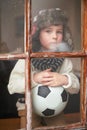 I wish the sun would come out already. a sad little boy holding a soccer ball while watching the rain through a window. Royalty Free Stock Photo