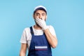 I won`t say anyone! Scared handyman in overalls and gloves covering mouth with hand, afraid to talk, looking intimidated Royalty Free Stock Photo