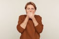 I won`t speak! Portrait of terrified young man in sweatshirt covering mouth and looking shocked intimidated