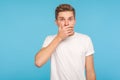 I won`t tell anyone! Portrait of scared man in white t-shirt covering mouth with hand to keep silent