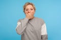 I won`t tell! Shocked intimidated woman in grey sweatshirt covering mouth with hand and looking scared at camera