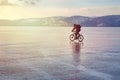 Ice biker traveler with backpacks on bike on ice of Lake Baikal. Against the background of sunset sky, ice surface. Winter sport
