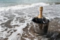 Ice bucket with champagne bottle and glasses on a beach surrounded by sea. Ocean waves chilling drinks, luxury vacation for two. Royalty Free Stock Photo