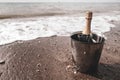 Ice bucket with champagne bottle and glasses on a beach surrounded by sea. Ocean waves chilling drinks, luxury vacation for two. Royalty Free Stock Photo