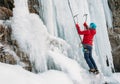 Ice climber dressed in warm winter climbing clothes, safety harness and helmet climbing frozen waterfall using two Ice climbing