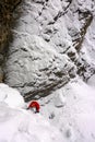 Ice climber in red jacket on a steep snow covered icefall in the Swiss Alps