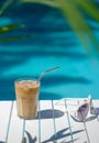 Ice coffee Cyprus Frappe Fredo against blue clear water of the swimming pool, on white table, with sunglasses . Summer Royalty Free Stock Photo