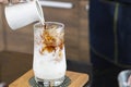 Ice coffee latte on a wooden table with black coffee being poured into it showing the texture and refreshing look of the drink