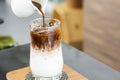 Ice coffee latte on a wooden table with black coffee being poured into it showing the texture and refreshing look of the drink