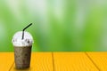 Ice Coffee in plastic take away cup with black straw on yellow wooden table on green nature blurry background, copy space Royalty Free Stock Photo