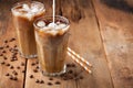 Ice coffee in a tall glass with cream poured over and coffee beans on a old rustic wooden table. Cold summer drink on a dark woode