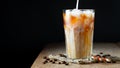 Ice coffee in a tall glass with cream poured over, ice cubes and beans on a old rustic wooden table. Cold summer drink