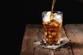 Ice coffee in a tall glass over and coffee beans on a old rustic wooden table. Cold summer drink on a dark background