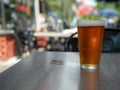 Ice cold amber beer sitting in a pint glass on a table outside with wet cup ring