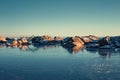 Ice covered fjord and colorful sky reflected in the ice. Winter landscape with islands, huts, sea, snowy rocks, blue sky Royalty Free Stock Photo