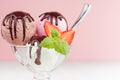 Ice cream balls different color - pink, brown, white with chocolate sauce, mint, spoon, strawberry slices in bowl on pink.