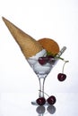 Ice cream balls with an inverted horn in a glass goblet with a round waffle, straw and cherry on a white background