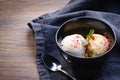 Ice cream balls or scoops in a black bowl on wooden table background. Asian homemade green tea and vanilla ice cream