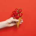 Ice cream cone filled with ripe strawberries isolated on red background. Hand holding Waffle cone with ripe strawberries Royalty Free Stock Photo
