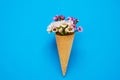 Ice cream cone with small flowers on blue background. Copy space, top view