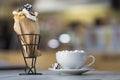 Ice cream dessert in wafer cup with chocolate cookies and and mug of coffee with marshmallows on porcelain plate on blurred Royalty Free Stock Photo