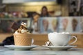 Ice cream dessert in wafer cup with chocolate cookies and and mug of coffee with marshmallows on porcelain plate on blurred Royalty Free Stock Photo