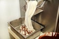 Ice cream making machine produces vanilla ice cream with chocolate dressing and it falls into steel container.