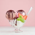 Ice cream scoops with slices strawberry, green mint, spoon, chocolate sauce in bowl in pink interior on white wood board.