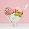 Ice cream scoops - strawberry, chocolate, creamy with slices fruit, green mint, spoon in bowl in pink interior on white wood.
