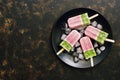 Ice cream on a stick is pink green.Strawberry ice cream on a stick on a black plate, dark background, top view, space for your tex
