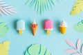 Ice cream on stick and in wafer cone with multicolored origami tropical leaves abstract on blue
