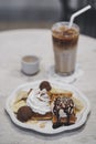 Ice cream. Vanilla ice cream topping with chocolate sauce and whipped cream on waffles. Blurred iced coffee on the background. Royalty Free Stock Photo