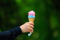 Ice cream waffle cone in hand on blurred green park background. Selective focus and copy space Royalty Free Stock Photo