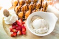 Ice cream in a white plate, strawberry waffles and whipped cream in a wooden tray on the table