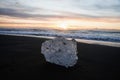 Ice crystal part piece iceberg glacial fragment on black sand ocean waves sunset Diamond Beach Jokulsarlon South Iceland