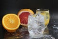 Ice cube flies falls into the takan with water soda next to lie orange grapefruit and ice on a black background. Refreshing drinks Royalty Free Stock Photo