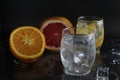 Ice cube flies falls into the takan with water soda next to lie orange grapefruit and ice on a black background. Refreshing drinks Royalty Free Stock Photo