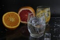 Ice cube flies falls into the takan with water soda next to lie orange grapefruit and ice on a black background. Refreshing drinks Royalty Free Stock Photo