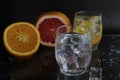 Ice cube flies falls into the takan with water soda next to lie orange grapefruit and ice on a black background. Refreshing drinks Royalty Free Stock Photo