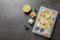 Ice cube tray with frozen fruits and mint on grey table, flat lay. Space for text Royalty Free Stock Photo