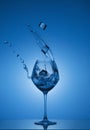 Ice cubes fall into a glass and water is poured out. Water splashing out of a tall wine glass. Royalty Free Stock Photo