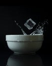 Ice cubes falling into white bowl on a black background stopped with high speed photography Royalty Free Stock Photo