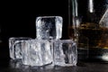 Ice cubes on a glass table close-up with water drops. A glass of whiskey in the background Royalty Free Stock Photo