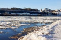 Ice drift on a river with blue high water and big water, white snow broken ice full of hummocks in it and city with houses at a Royalty Free Stock Photo