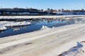 Ice drift on a river with blue high water and big water, white snow broken ice full of hummocks in it and city with houses at a Royalty Free Stock Photo