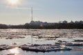 Ice drift on a river with blue high water and big water, white snow broken ice full of hummocks in it and city with houses at a Royalty Free Stock Photo