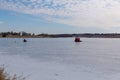 Ice fishing; frozen lake surface in winter with ice fisherman and an ice shanty on the lake.