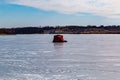 Ice fishing; frozen lake surface in winter with a red ice shanty or ice hut on the lake.