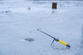 Ice fishing rod ready waiting for fish bite in a hole on a narrow frozen river, wet surface during March thaw