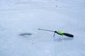 Ice fishing rod waiting for fish bite in a hole on a frozen river, wet surface detail during March thaw popular season